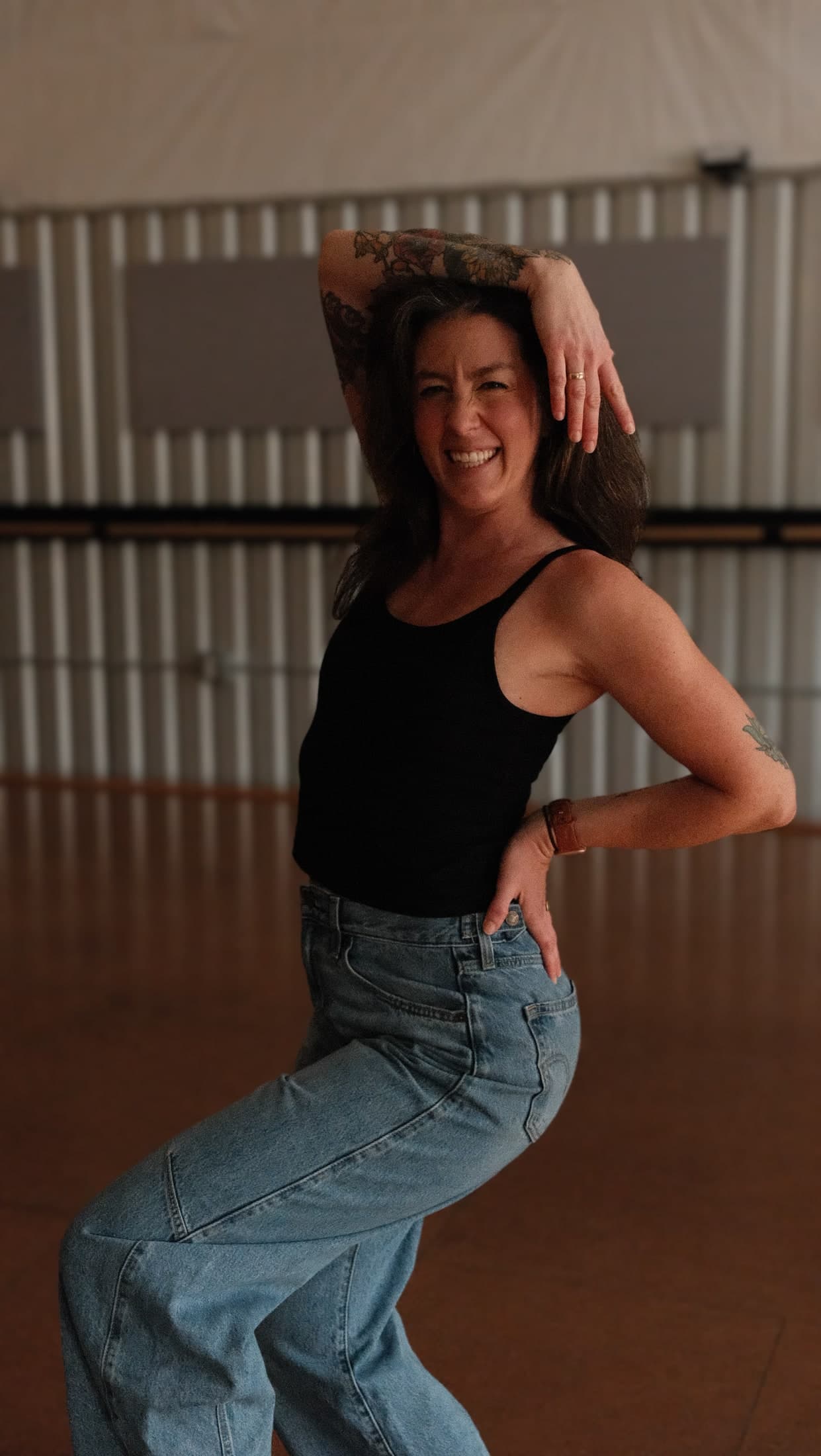 Leigh grooving barefoot in a black tank top and jeans, one arm draped overhead.