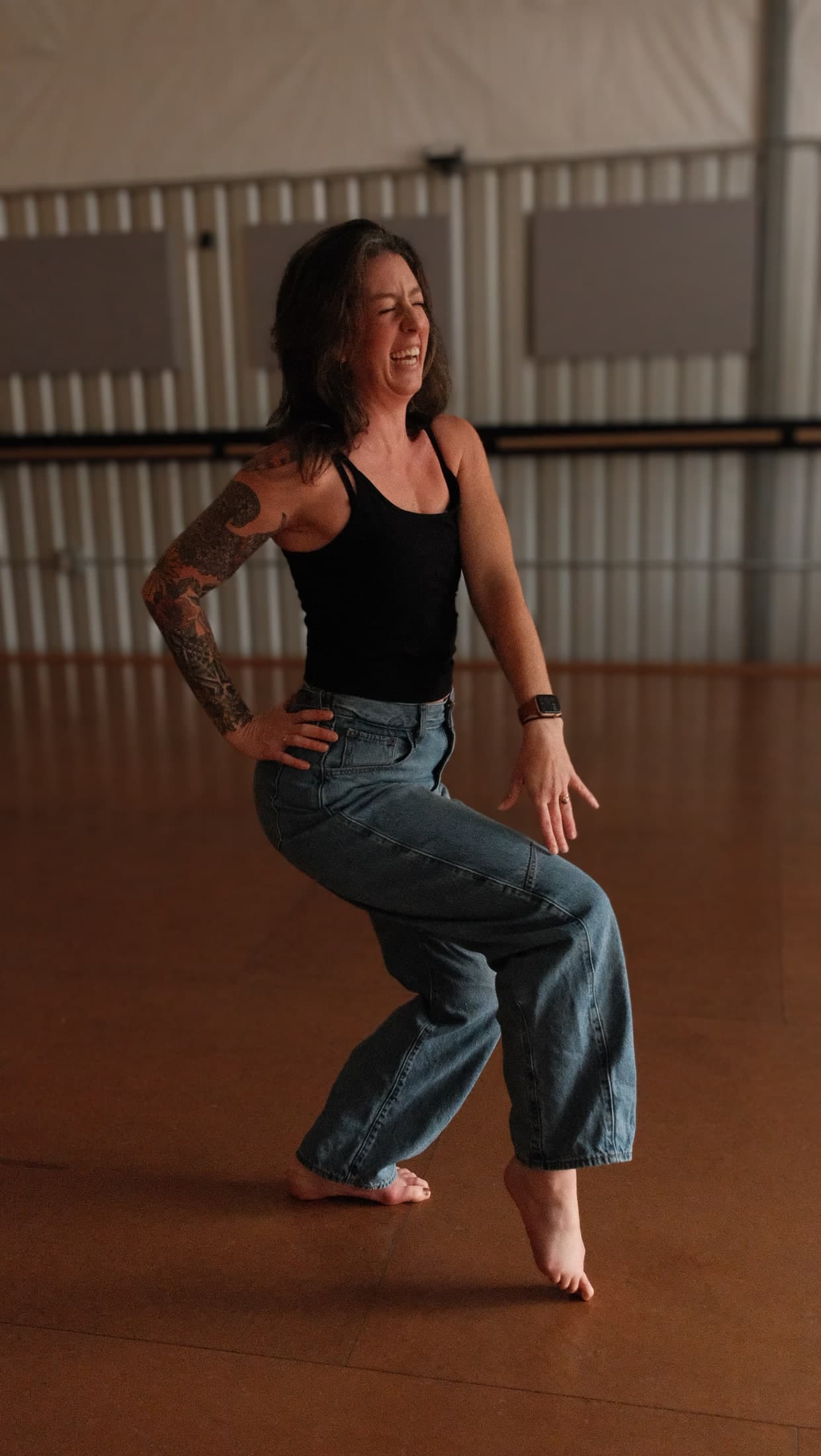 Leigh laughing mid-dance, up on the balls of her feet in a warm studio.