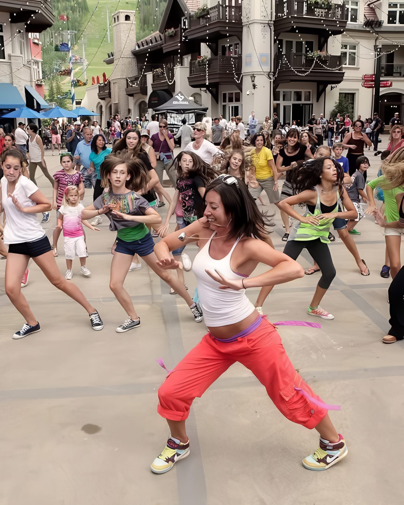 A big outdoor group dance class in full swing — dozens of people following the instructor across a village plaza under strings of lights.